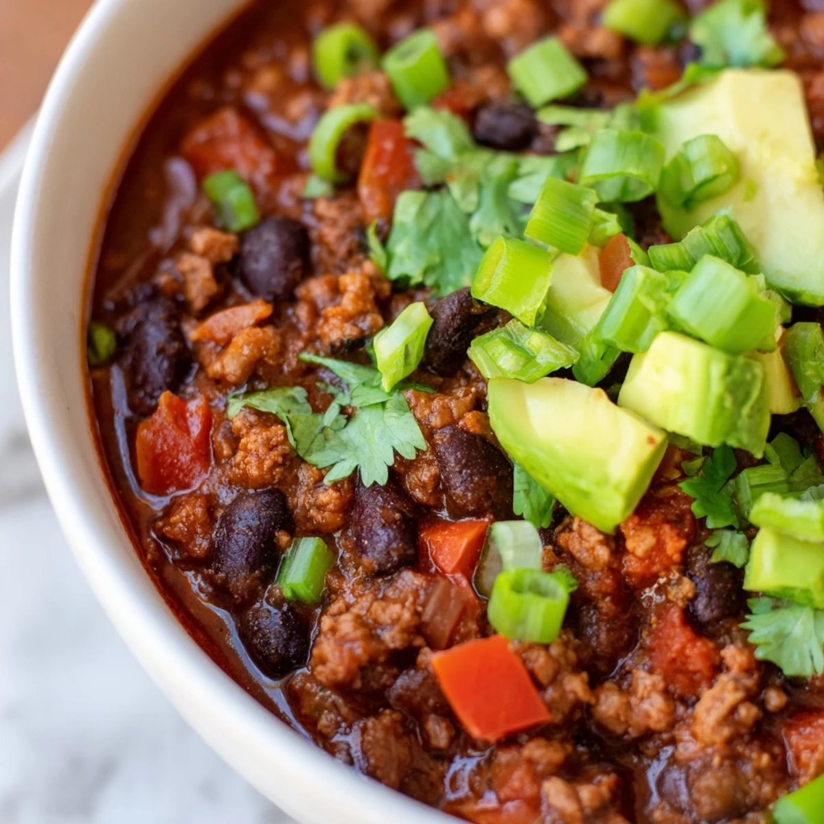 A warm bowl of Turkey Chili with Black Beans and Tomatoes garnished with fresh cilantro and diced avocado.