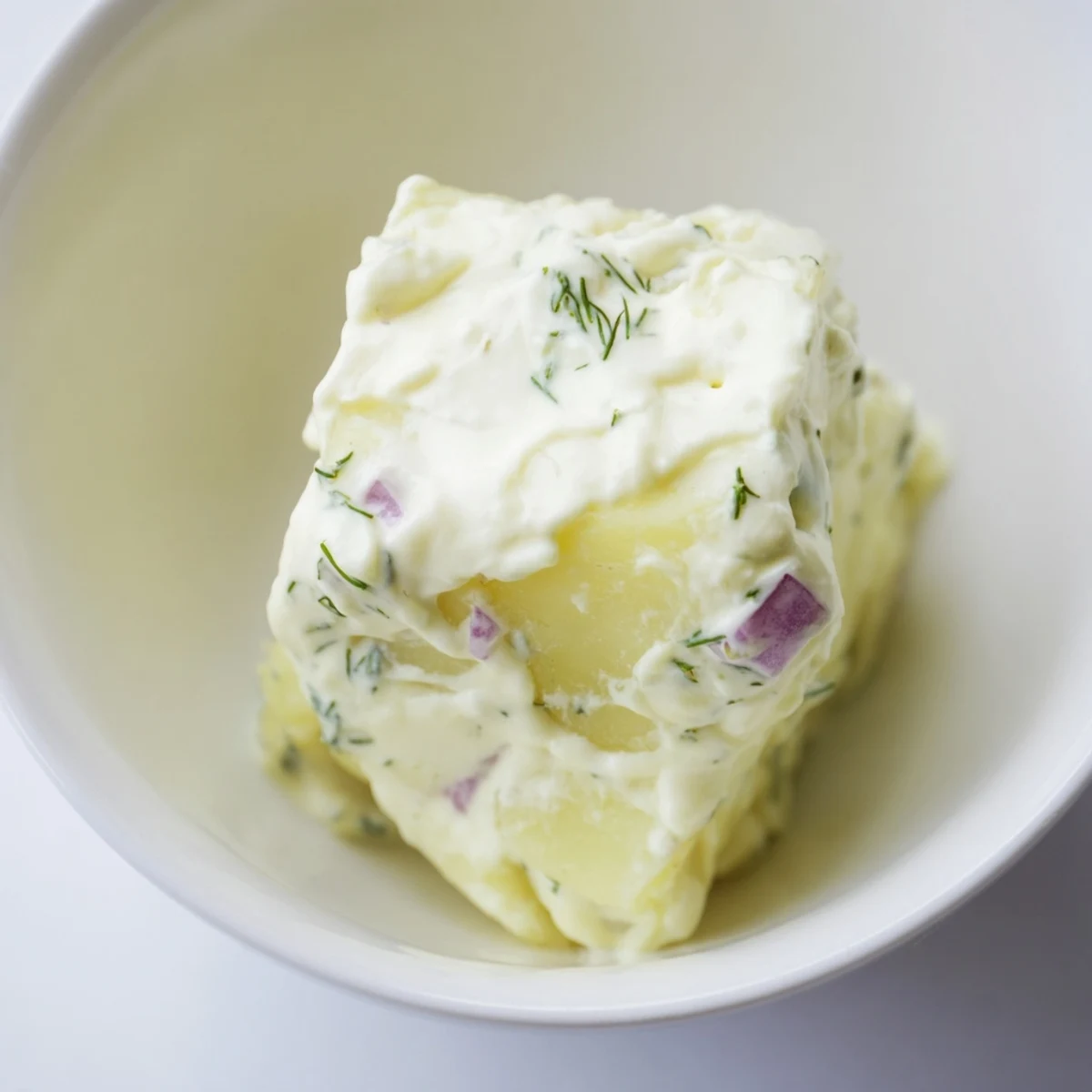 Overhead view of homemade Creamy Potato Salad with Fresh Dill, garnished with sprigs and red onion specks.