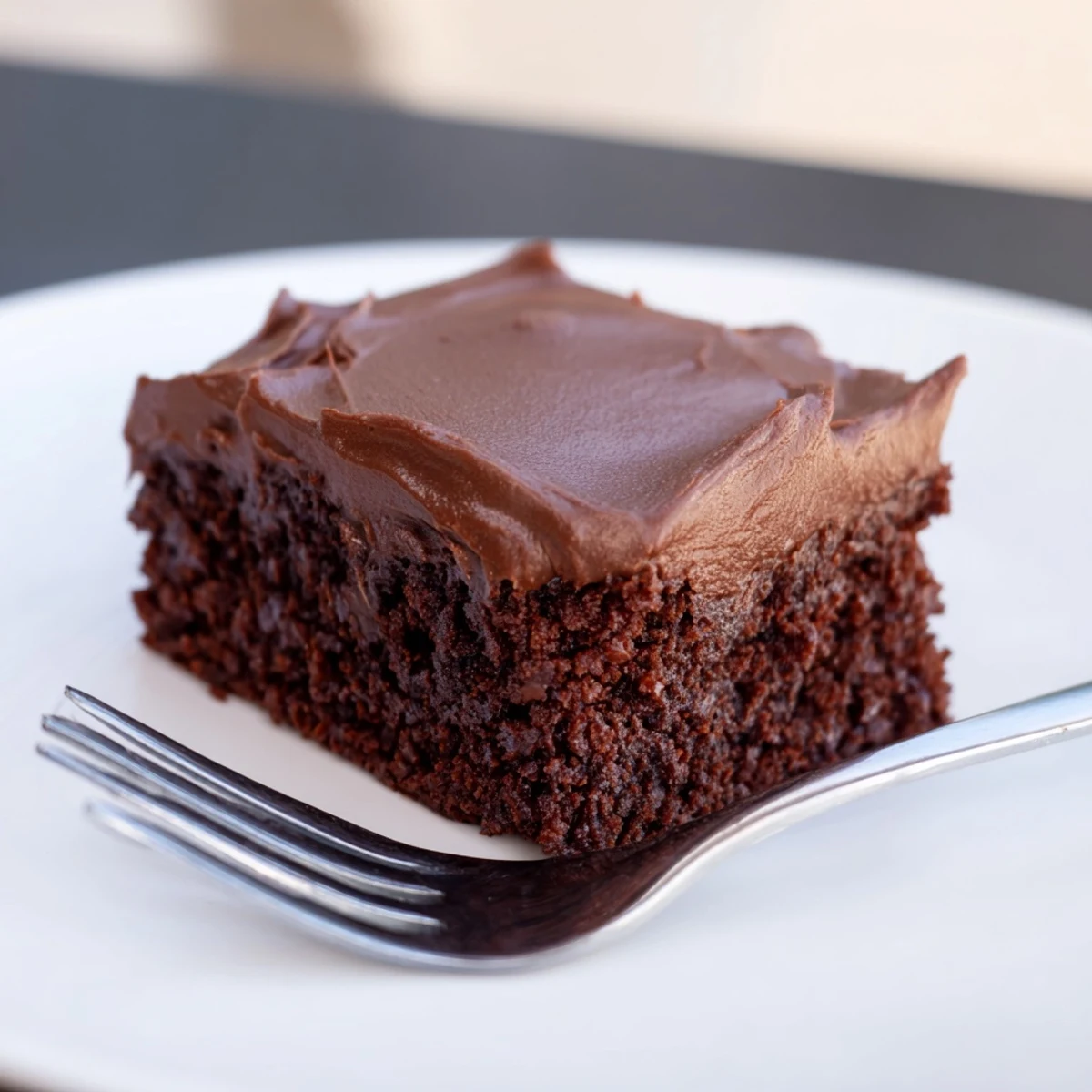 A hand holds a freshly cut square of Chocolate Brownies with Rich Fudge Frosting, revealing a moist interior and a side of melting vanilla ice cream.