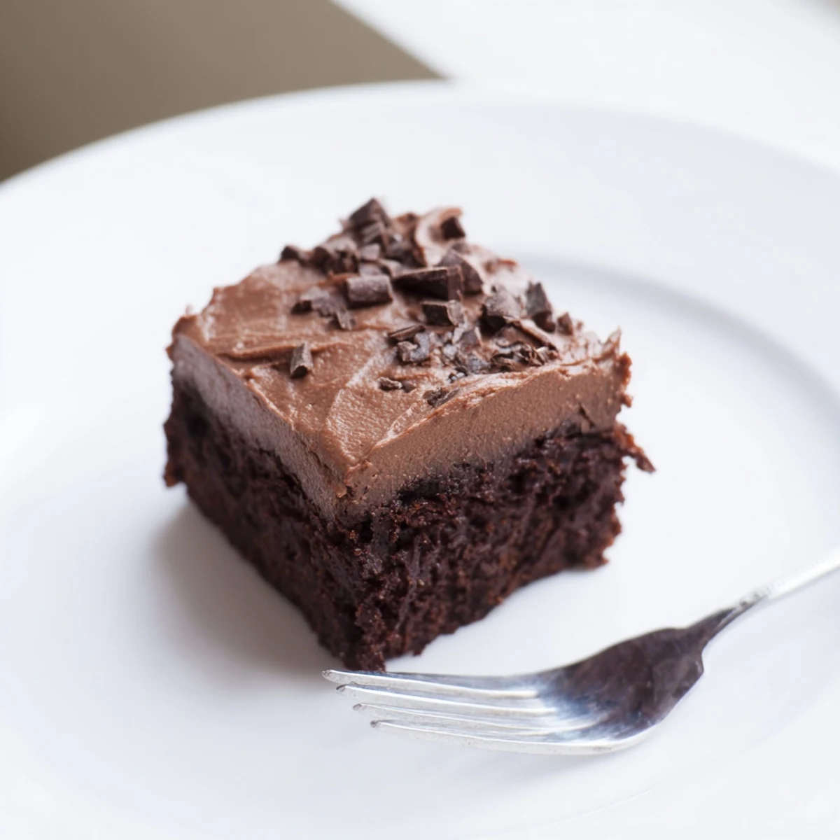 A close-up shot shows a stack of chocolate squares, highlighting the dense, fudgy texture and the thick, creamy layer of homemade fudge frosting.