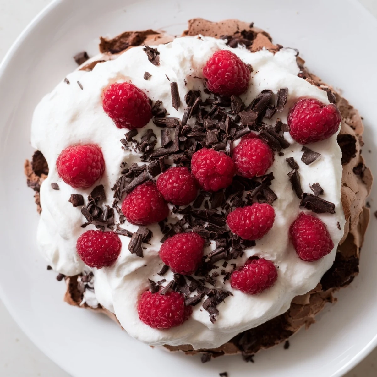 A slice of Chocolate Raspberry Pavlova reveals the crackly chocolate meringue base, topped with billowy whipped cream and fresh raspberries.