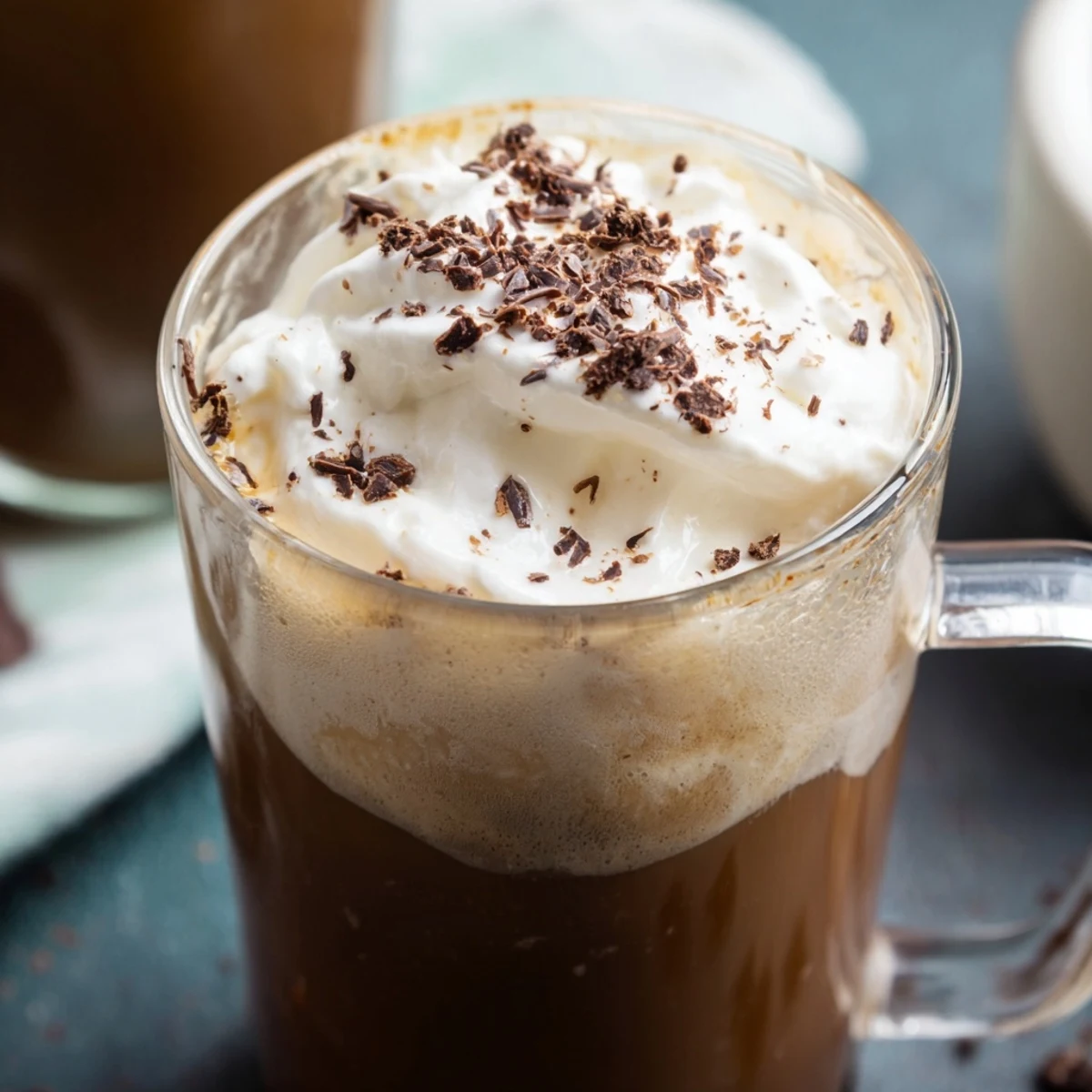 Golden light highlights a creamy Irish Coffee Mocktail, garnished with dark chocolate shavings on a wooden coaster.