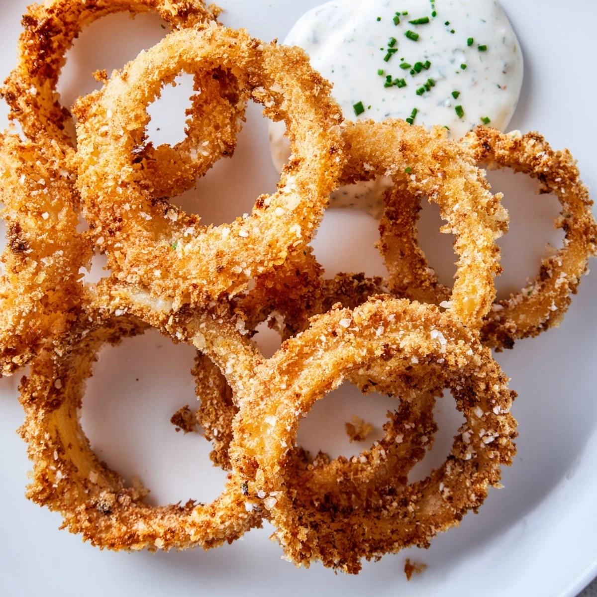 Savory Touchdown Crispy Onion Rings on a platter, garnished with herbs alongside a dip of ranch.