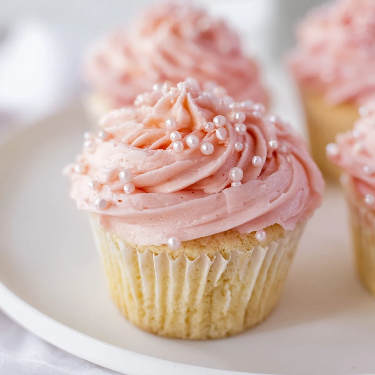 Freshly baked Pink Champagne Cupcakes, topped with light pink buttercream and edible pearls, sitting on a marble countertop.