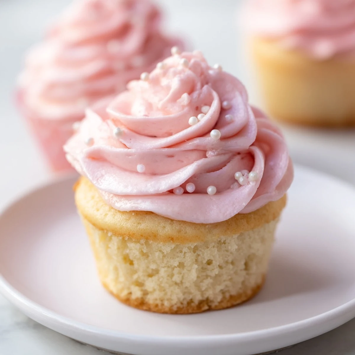 Close-up view of Pink Champagne Cupcakes, revealing their fluffy texture and glossy, pastel pink frosting swirls.
