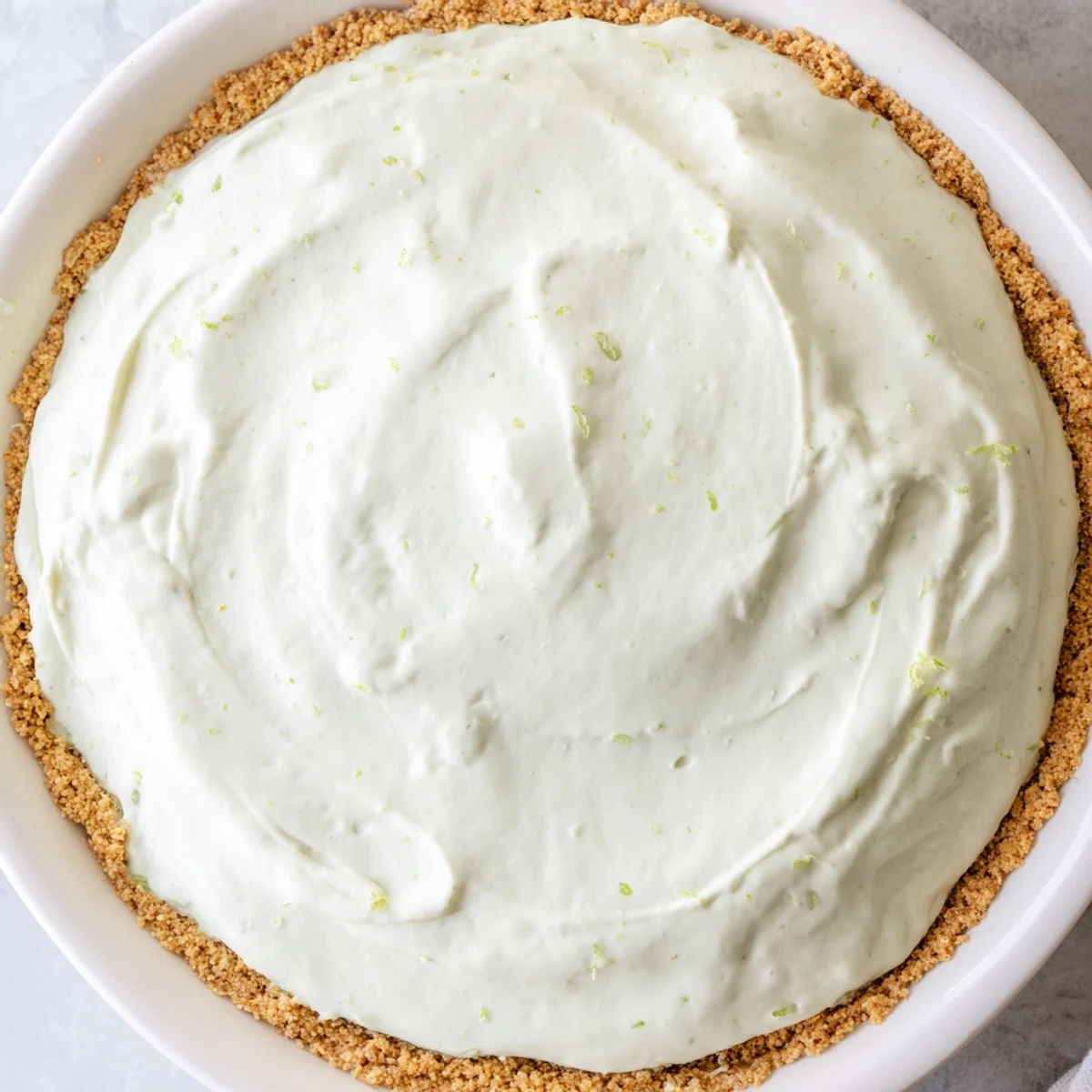 Golden-brown graham cracker crust cradles creamy Key Lime Pie with Whipped Cream Topping garnished with fresh lime zest.  