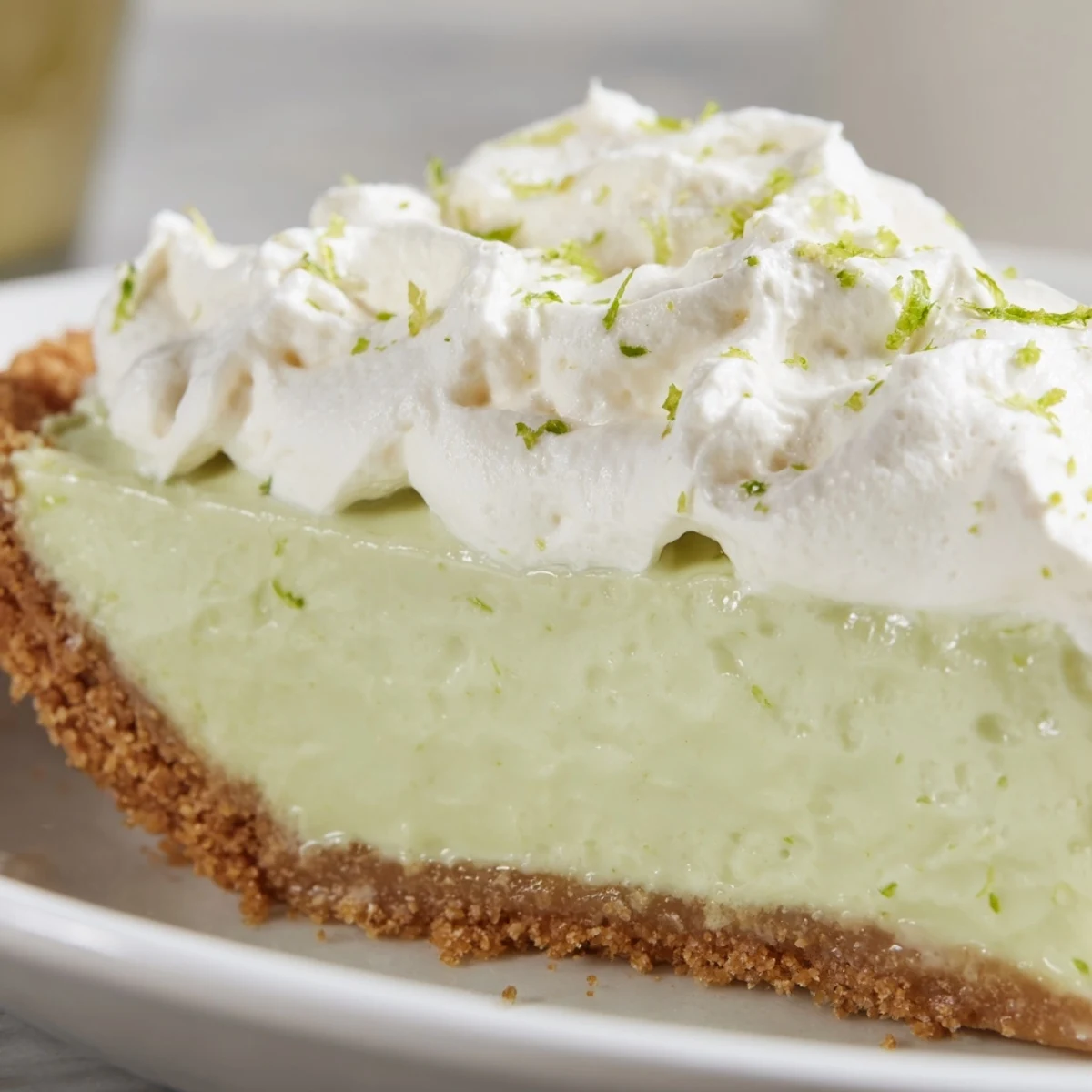 A close-up of Key Lime Pie with Whipped Cream Topping reveals billowy peaks of cream and buttery crumbs on the slice.