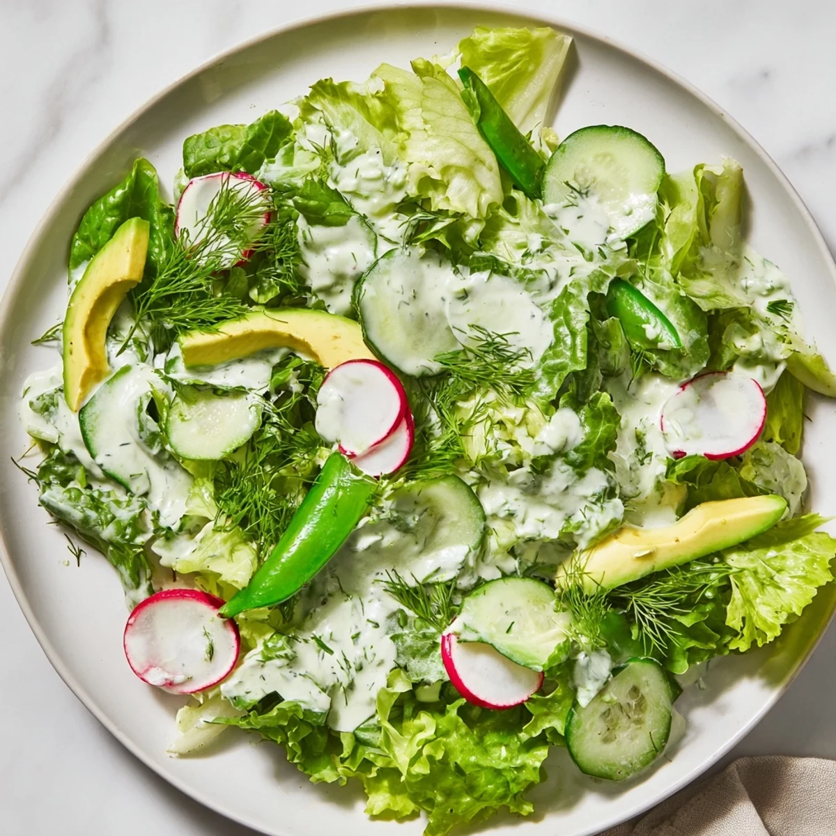 Freshly chopped mixed greens and crisp cucumbers tossed in vibrant Green Goddess dressing on a white plate.  