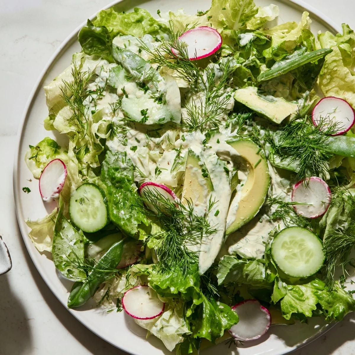 Green Goddess salad with creamy avocado slices, radishes, and snap peas glistening with herbaceous dressing.  