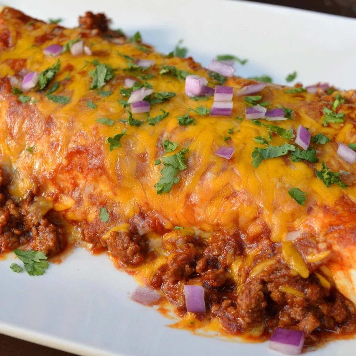 A close-up of Beef Enchiladas with Homemade Red Sauce bubbling with melted cheese in a baking dish.