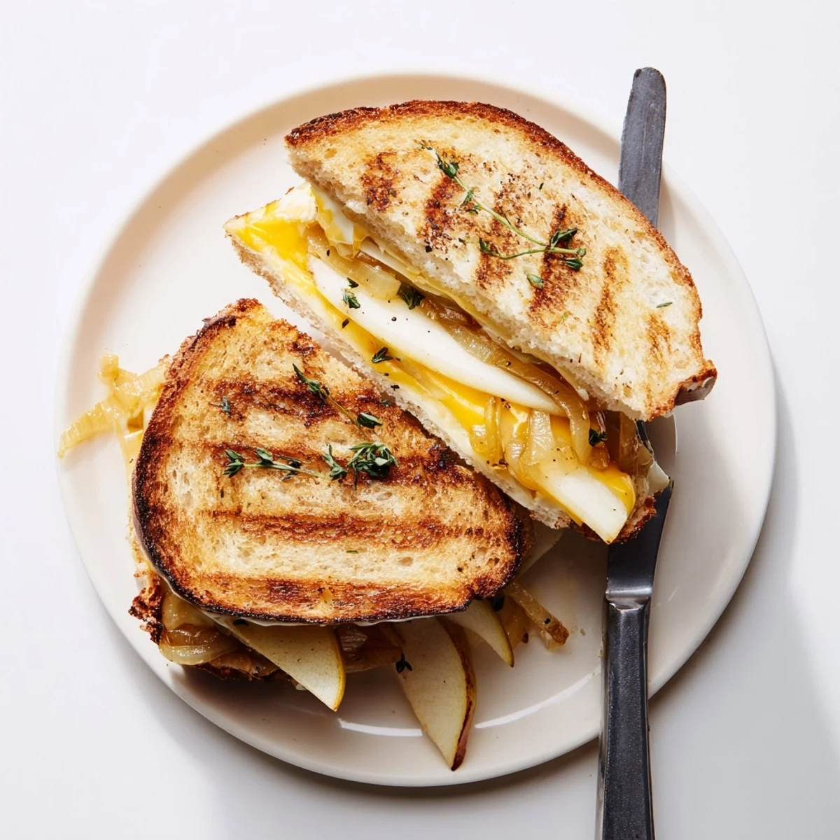 Close-up of a warm, buttery grilled sandwich, revealing melted cheddar, thinly sliced pear and apple, and rich caramelized onion layers.