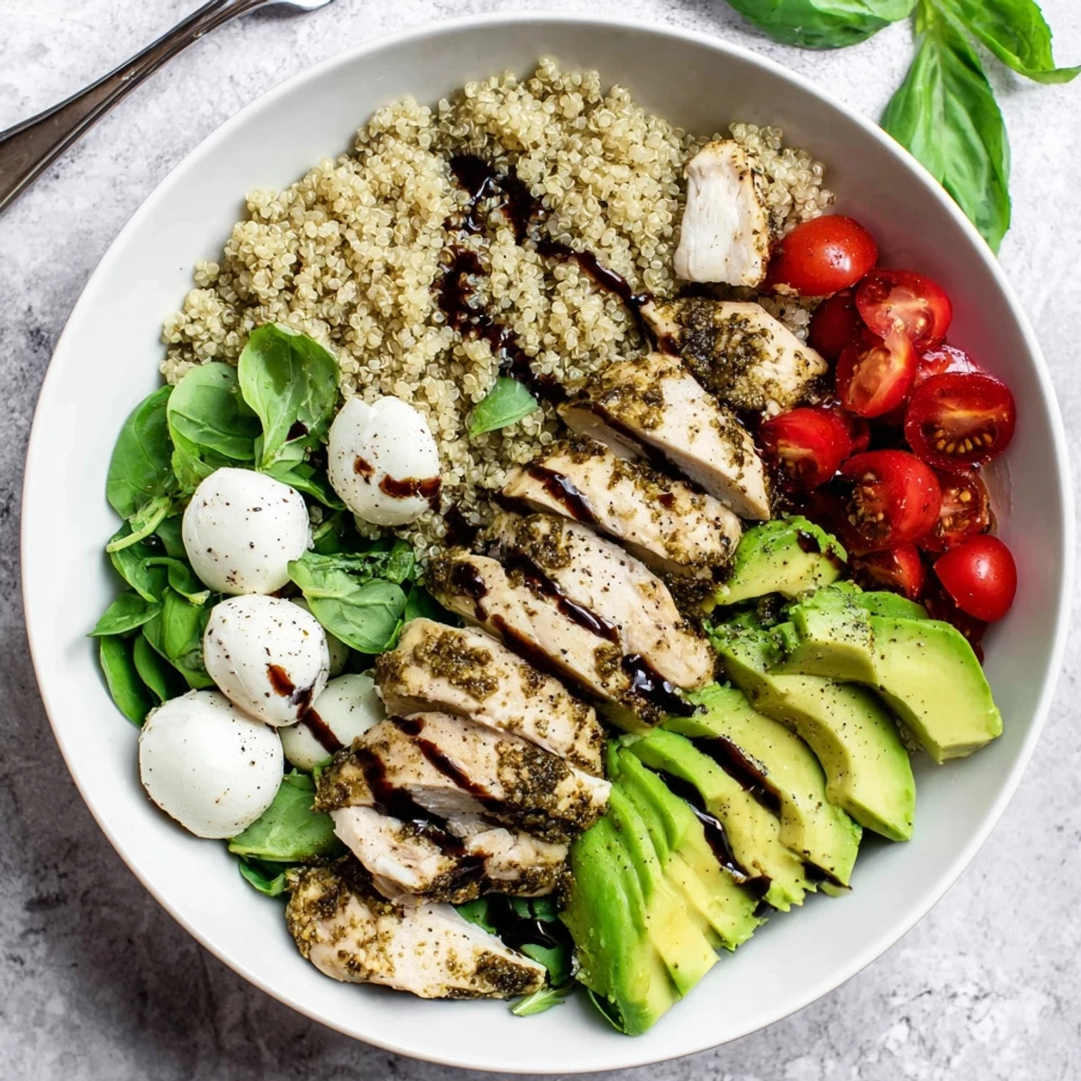 Juicy pesto chicken Caprese grain bowl with mozzarella, tomatoes, basil, avocado, and balsamic drizzle.