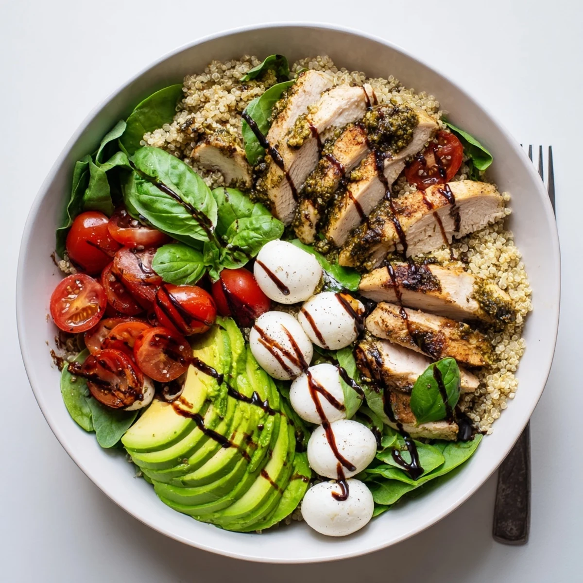 A vibrant pesto chicken Caprese grain bowl with arugula, avocado, and balsamic glaze, ready to enjoy.