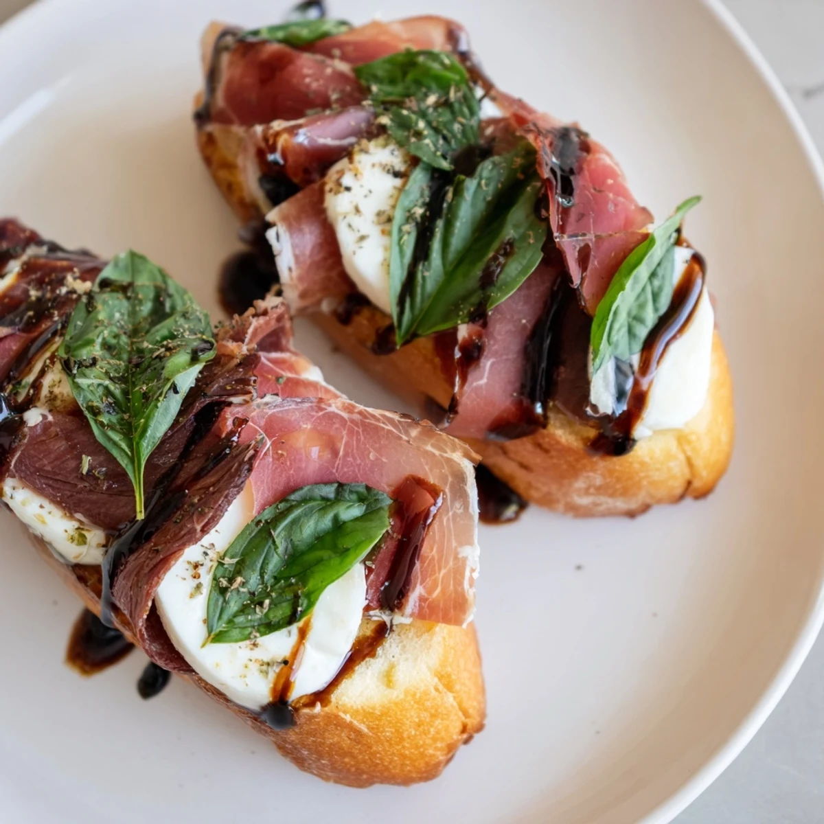 Crispy baguette slices with melted mozzarella, roast beef, prosciutto, basil, and balsamic glaze for a perfect appetizer.