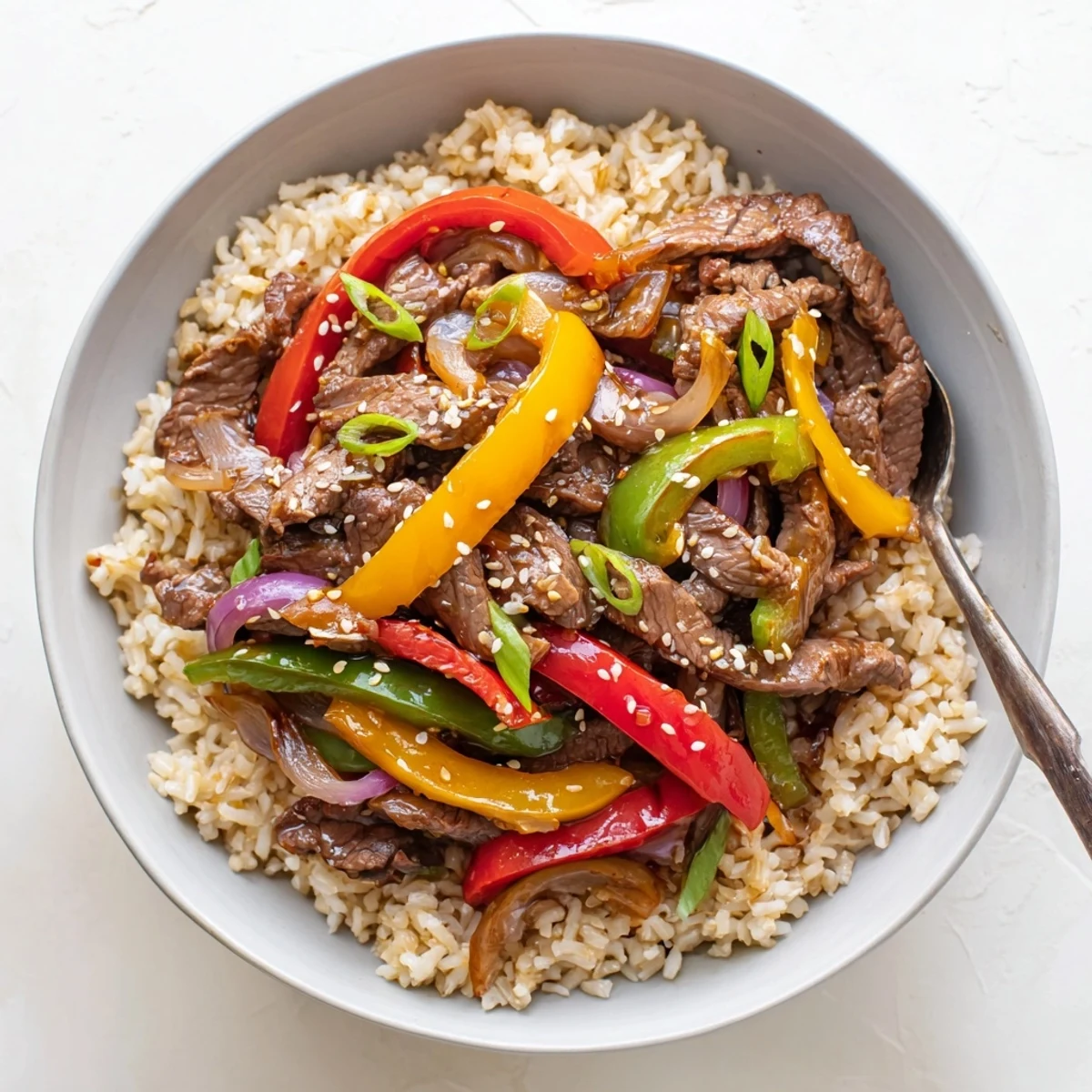 Healthy beef and pepper rice bowl topped with tender sliced beef and colorful crisp bell peppers