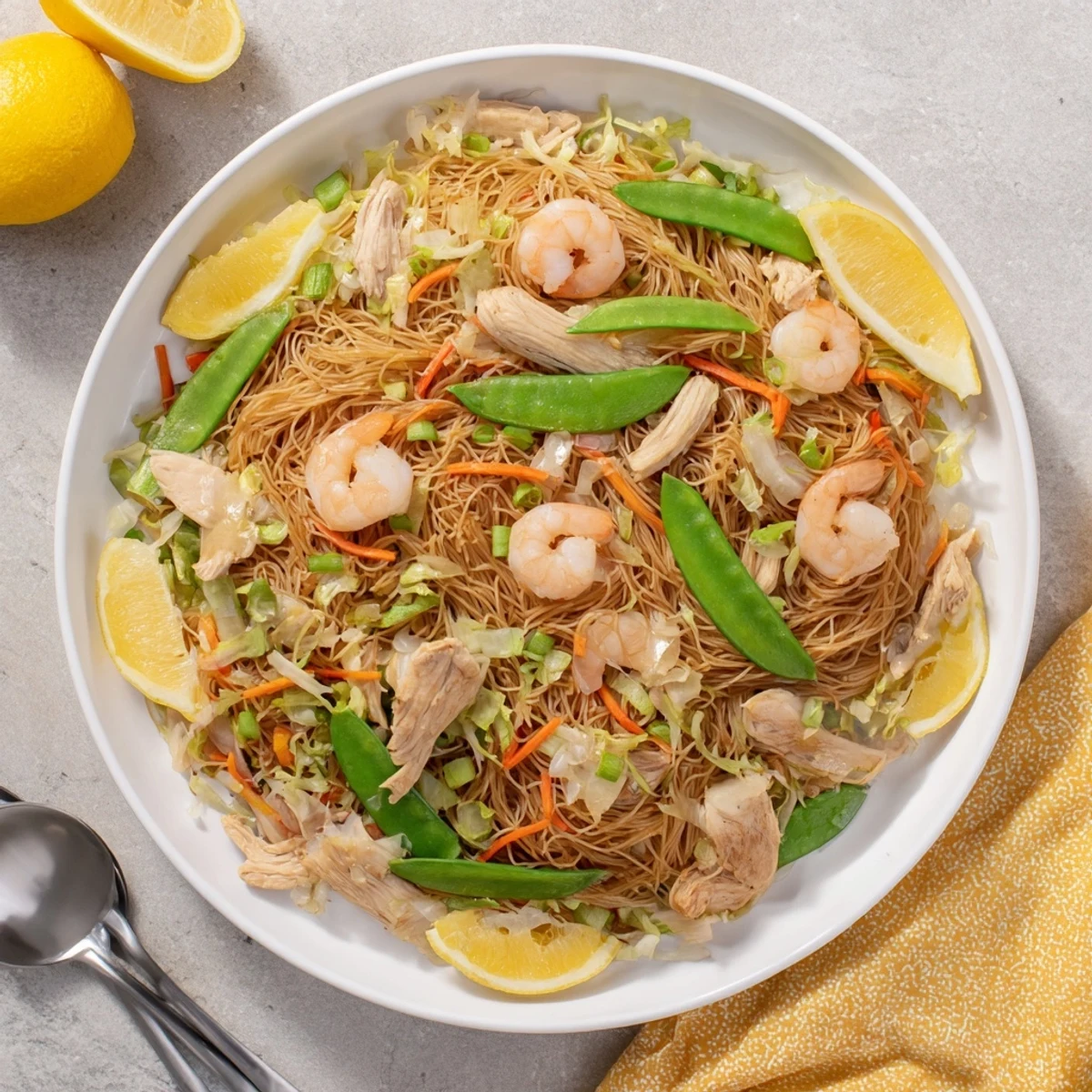 Steamy plate of traditional Pancit Bihon garnished with fresh scallions and served alongside bright lemon wedges for a tangy finish