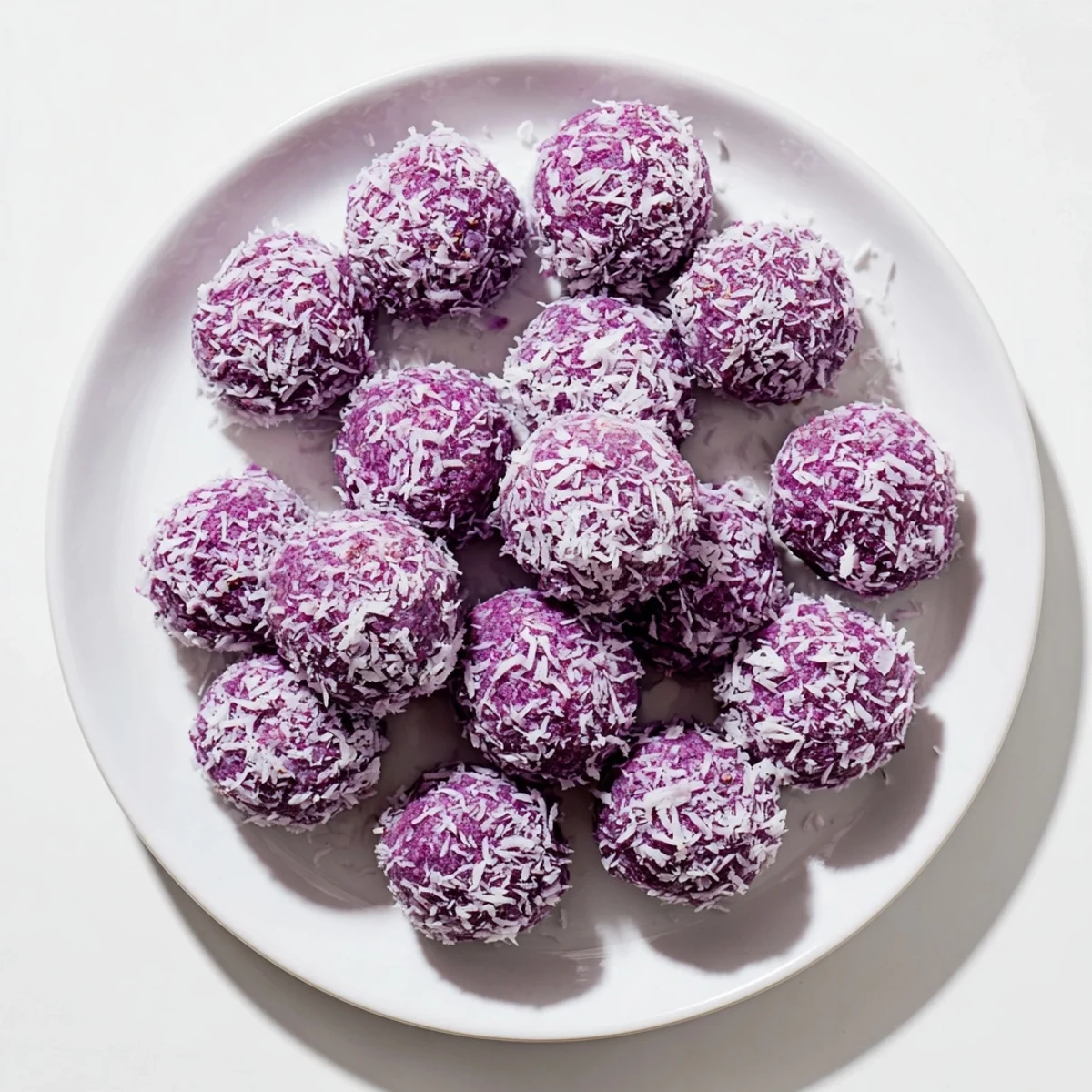 Bite-sized Coconut Ube Besito Cookies rolled in coconut, displaying their tender purple center