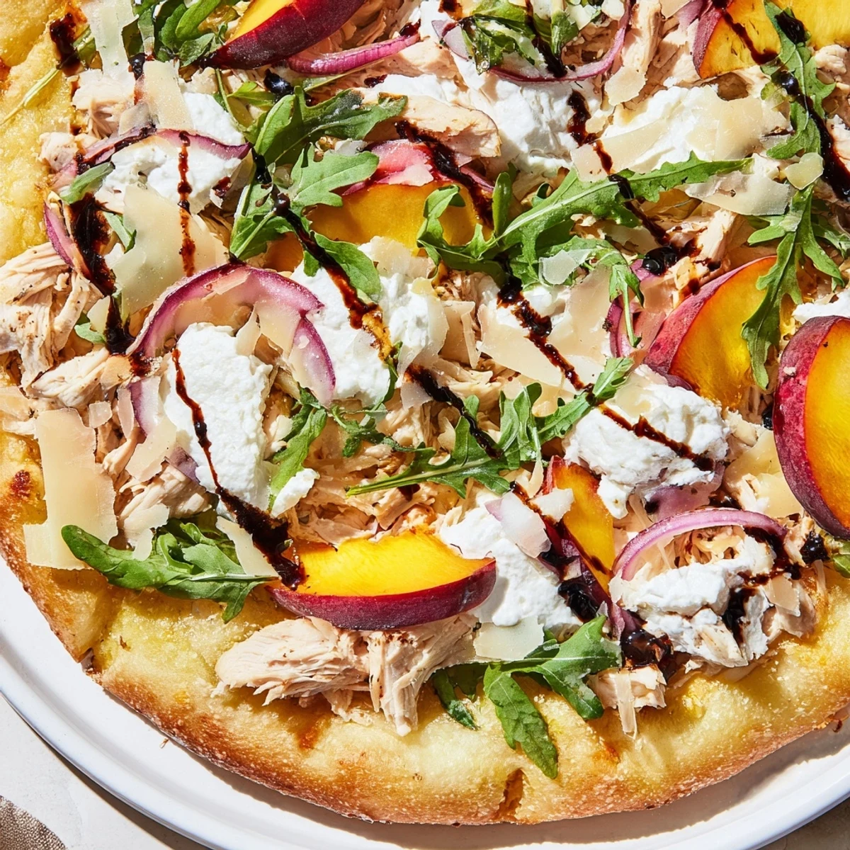 Chicken peach ricotta pizza drizzled with sweet balsamic glaze and finished with fresh arugula topping