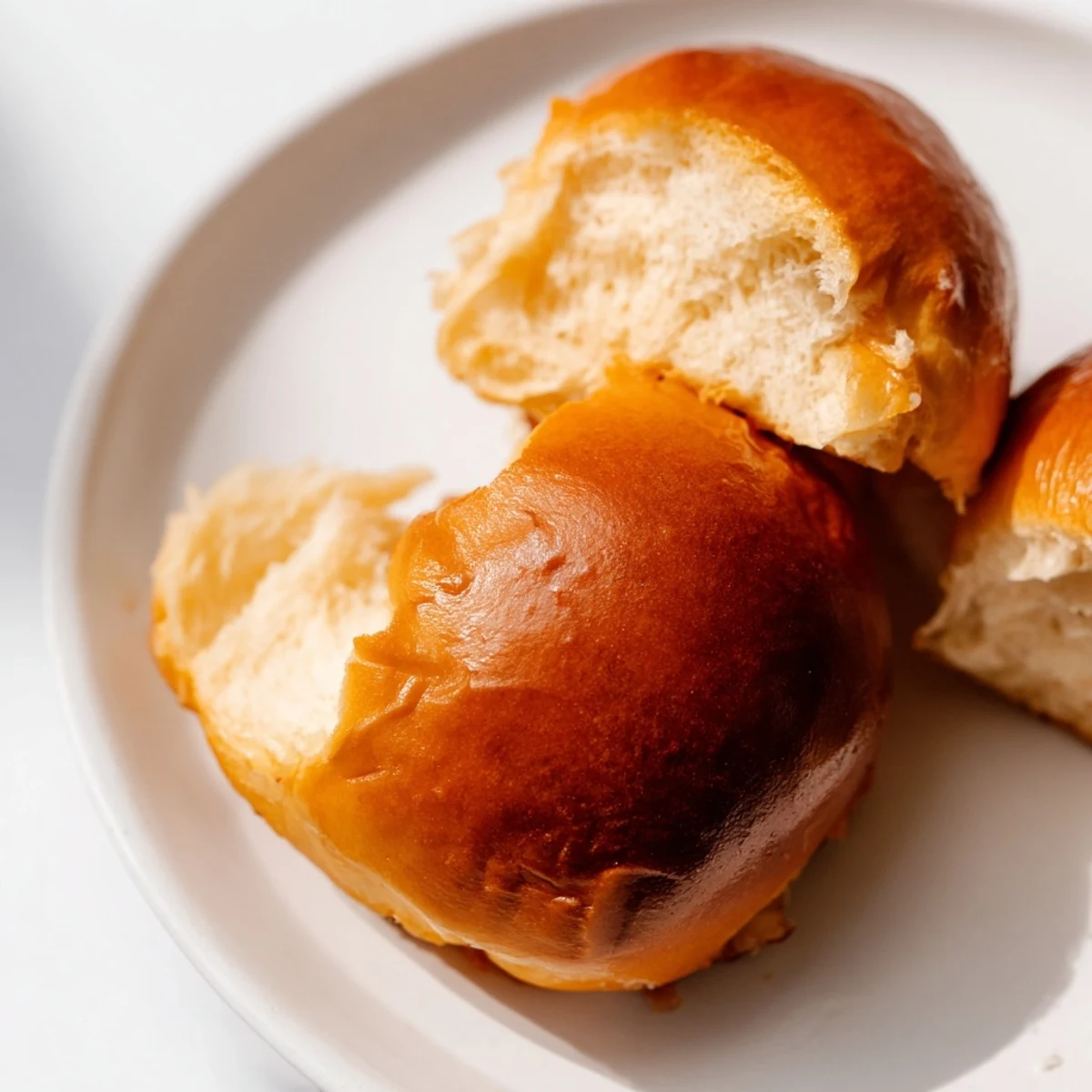 Golden brown brioche rolls with glossy tops and pillowy soft interiors on a wire rack