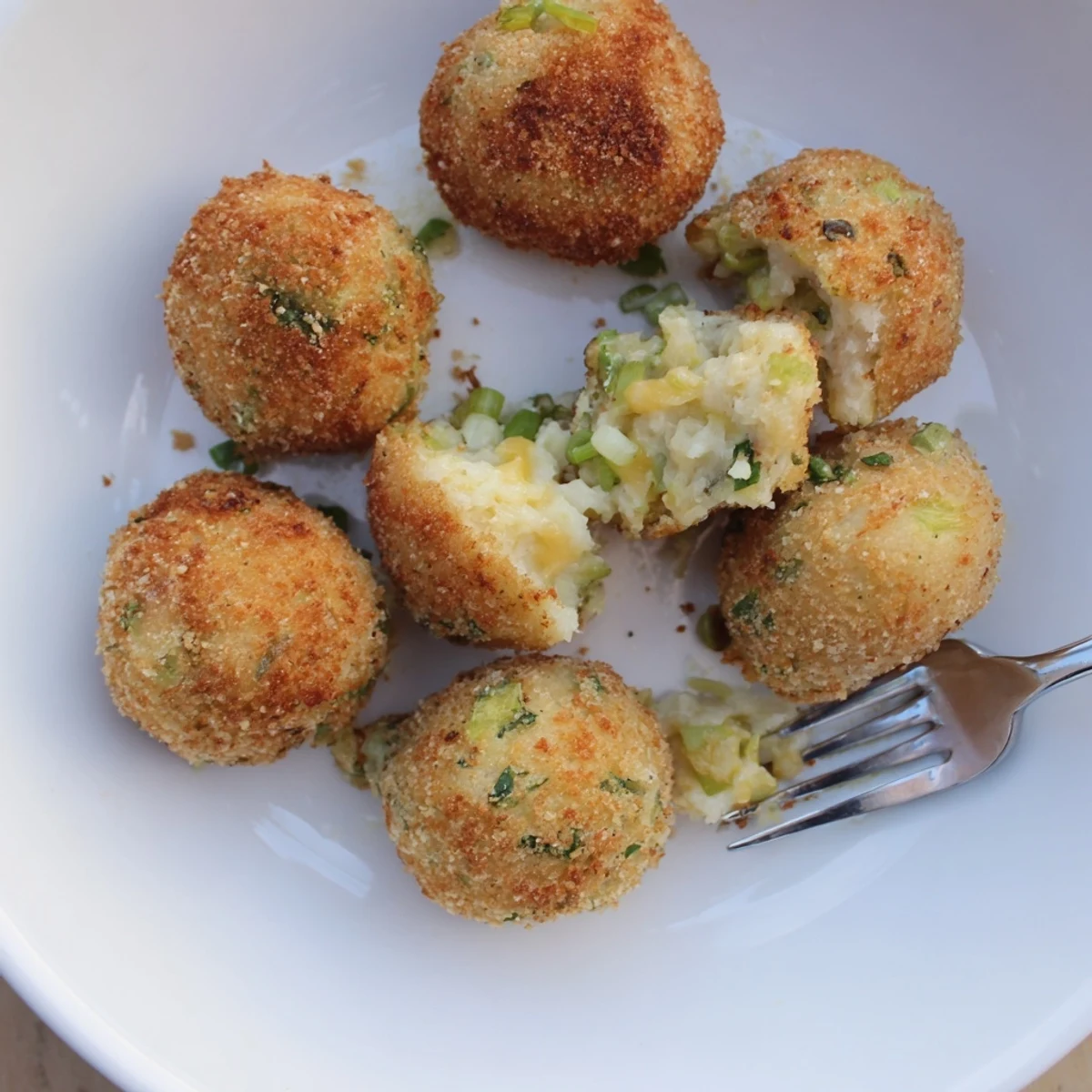 Golden brown crispy cheesy fried colcannon balls served on a white plate with dipping sauce