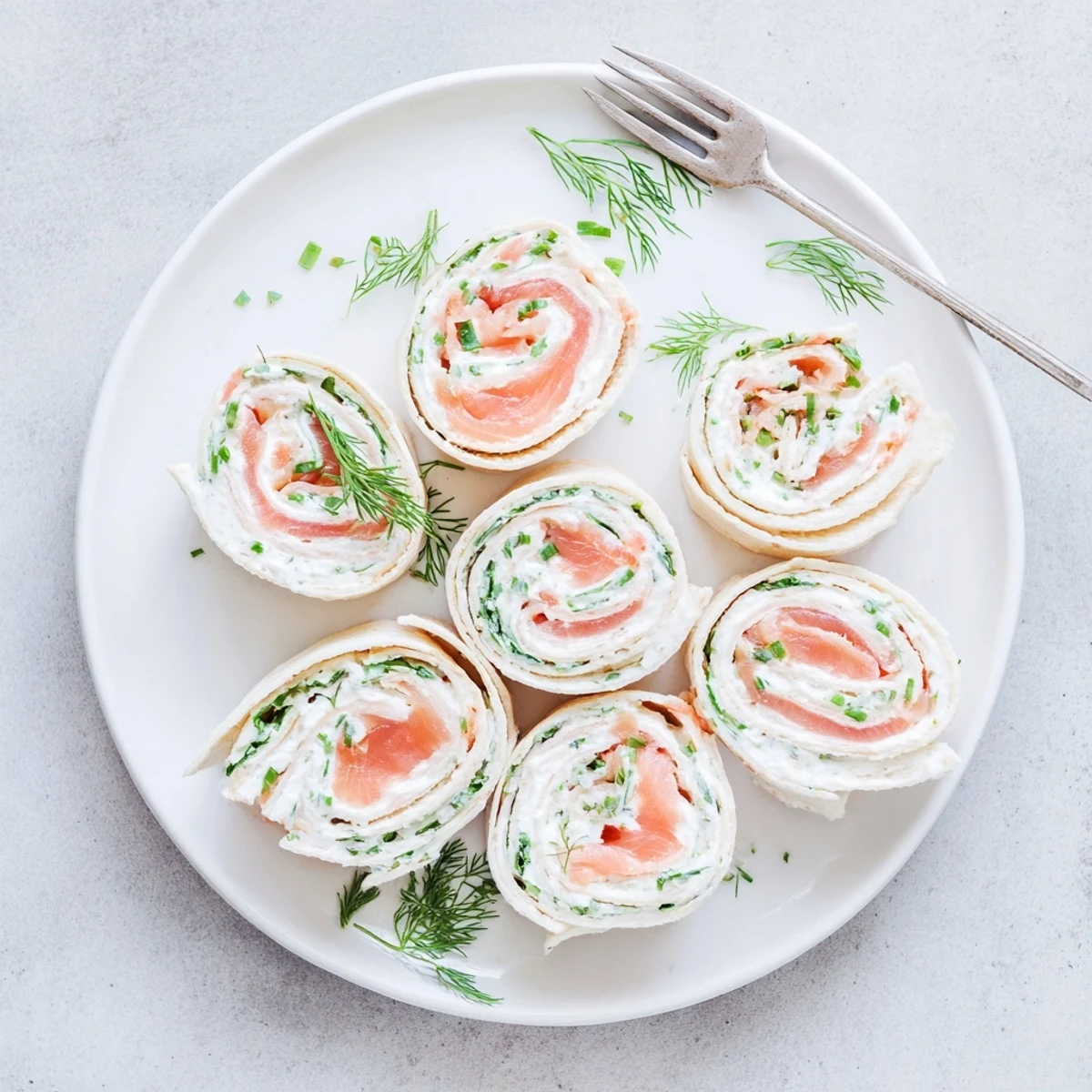 Golden spiral-cut smoked salmon roll ups with creamy herb cheese center on white platter