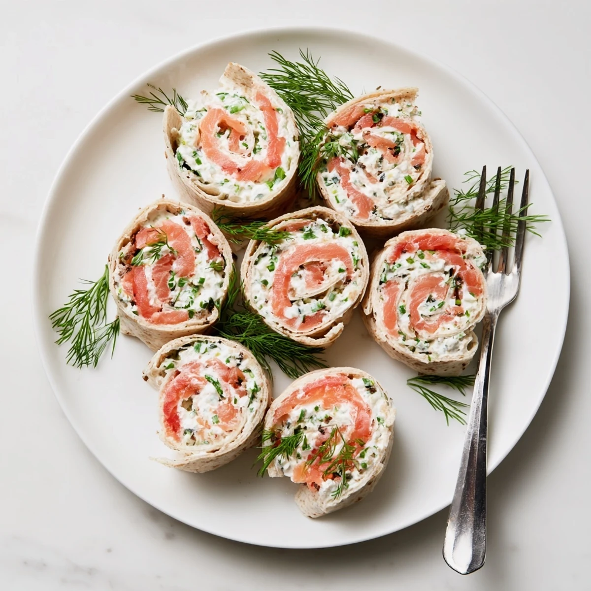 Appetizer platter featuring sliced smoked salmon roll ups with fresh dill and chive garnish
