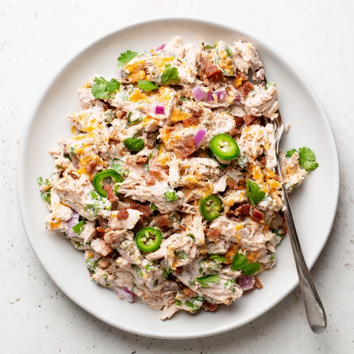 Creamy keto chicken salad loaded with crispy bacon, diced jalapenos, and shredded cheddar in a white serving bowl