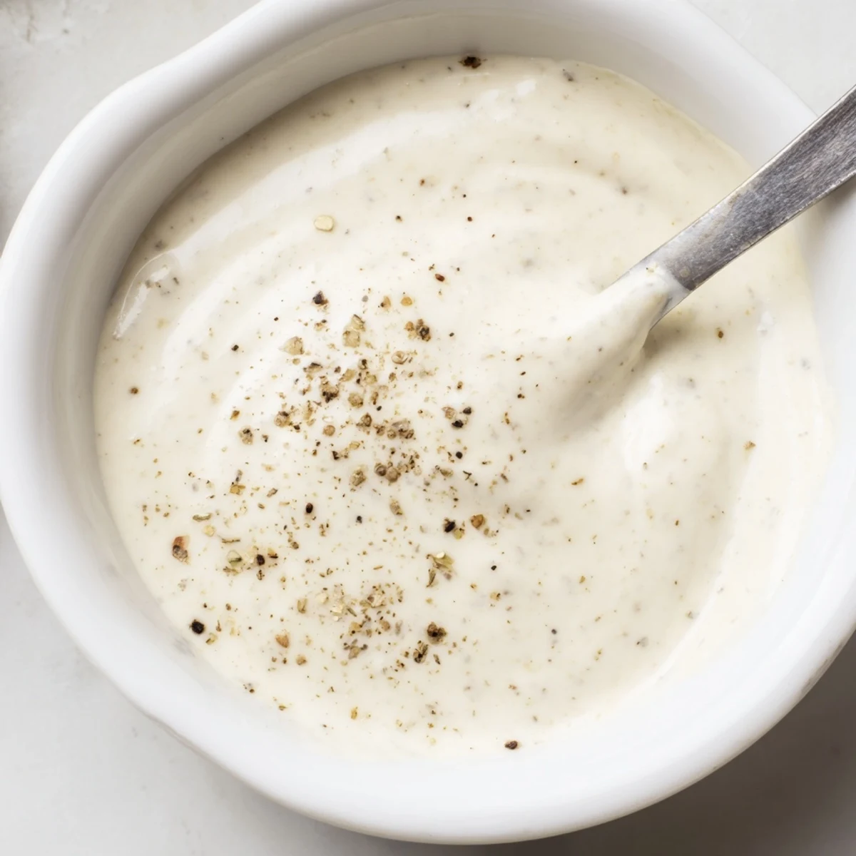 Smooth homemade chicken shawarma garlic sauce served in a small white dipping bowl beside fresh vegetables