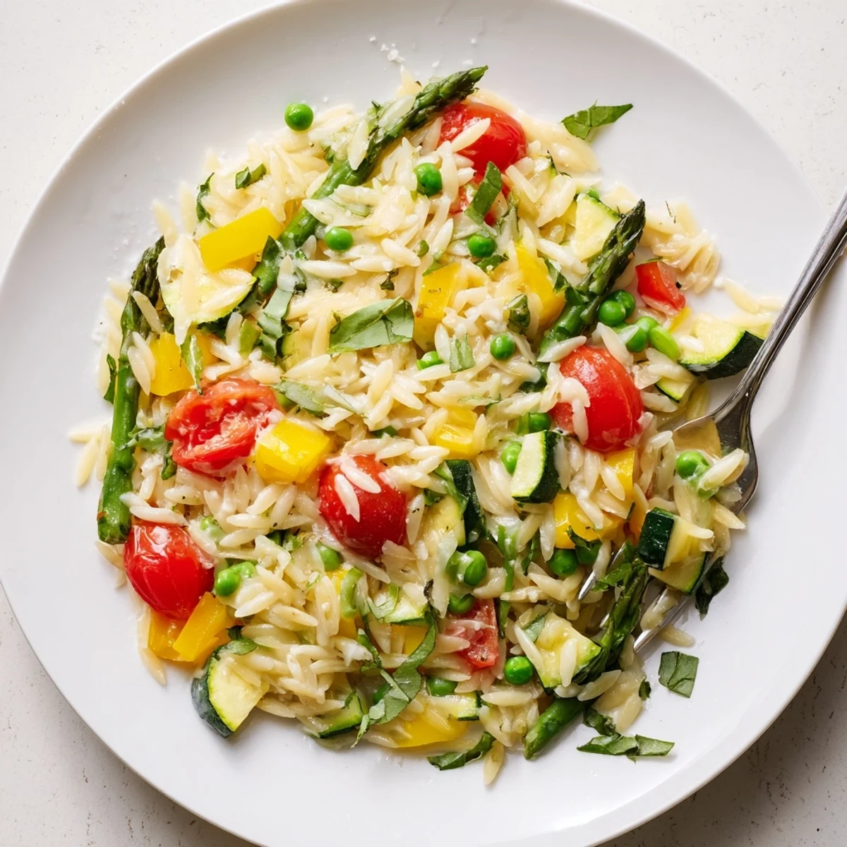 Steaming bowl of Orzo Primavera garnished with herbs, bright peas, and bell peppers
