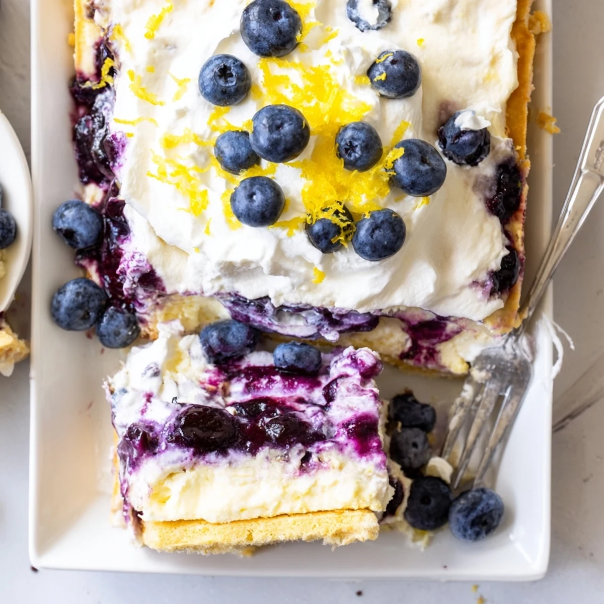 Thick slices of lemon blueberry lasagna topped with whipped cream and fresh berries