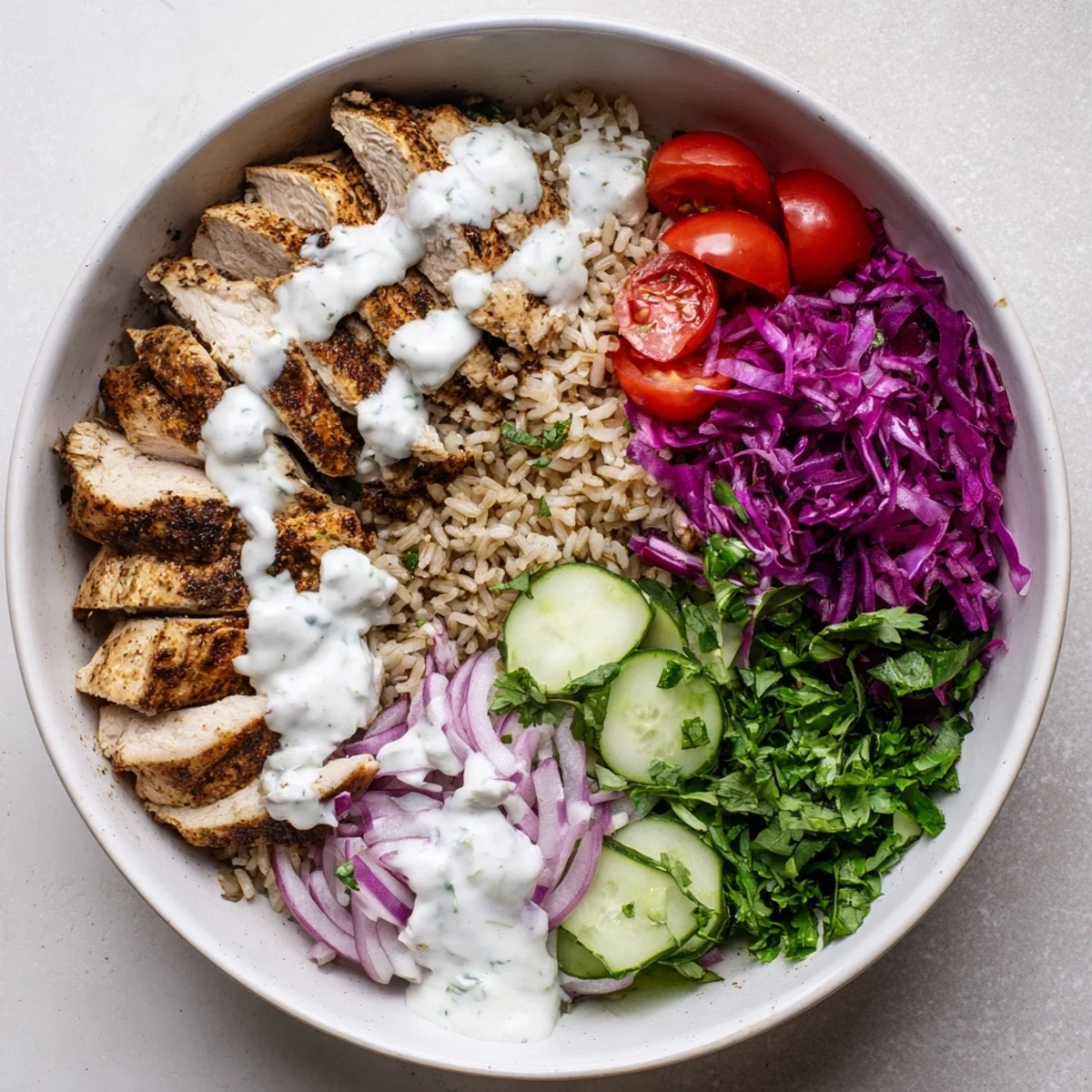 Golden spiced chicken slices atop colorful vegetables and fluffy grains drizzled with creamy tahini yogurt sauce