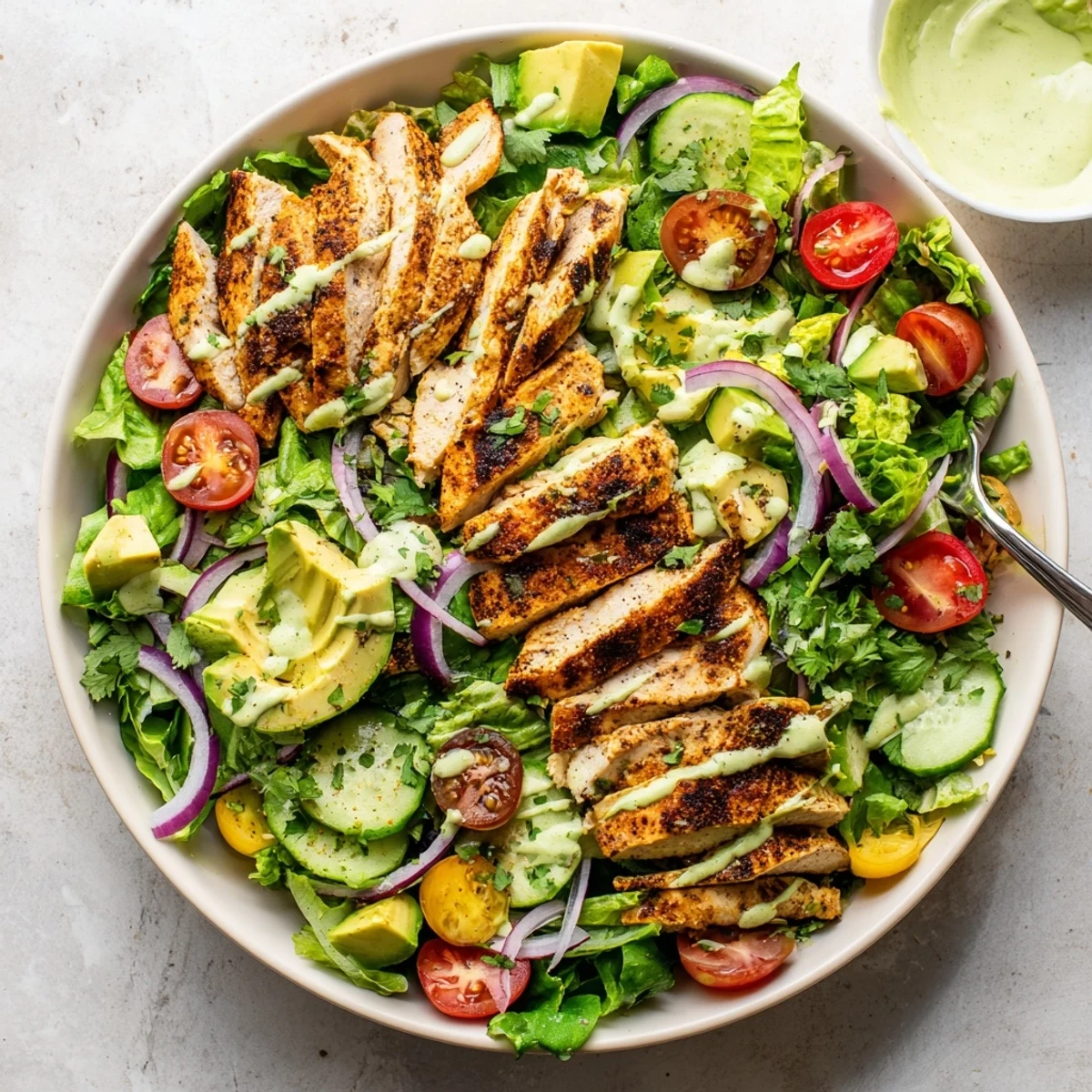 Golden grilled chicken slices atop mixed greens with diced avocado and creamy avocado lime dressing
