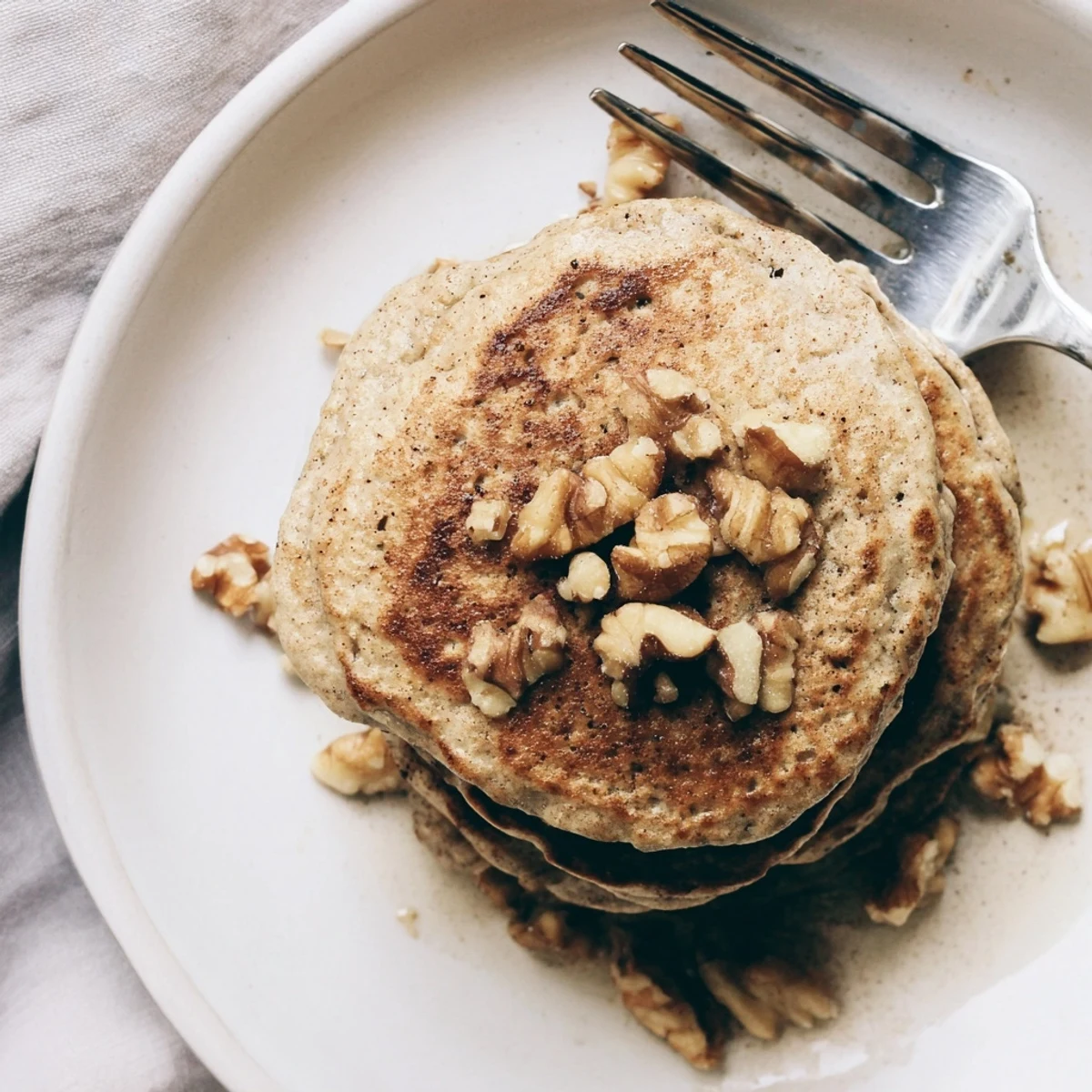 Stack of healthy protein banana pancakes on a white plate topped with blueberries and honey