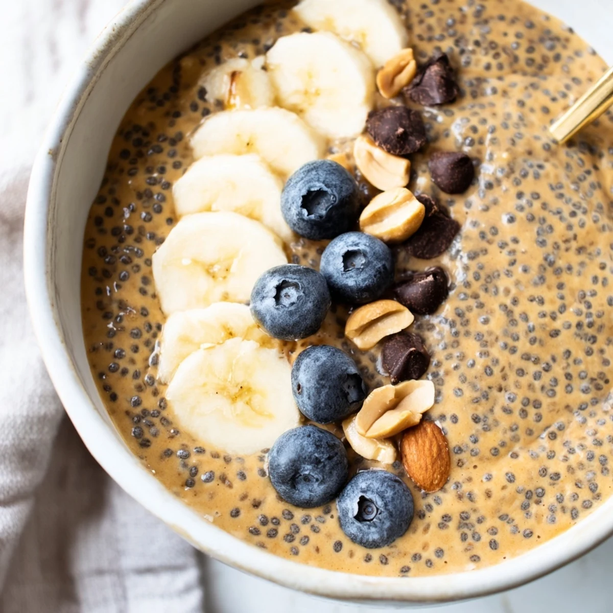 Thick peanut butter chia pudding topped with sliced banana and roasted peanuts