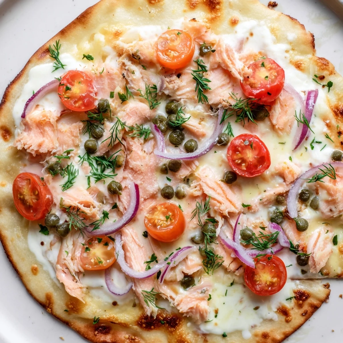 Golden baked salmon tortilla pizza with capers, red onion, and bubbling cheese