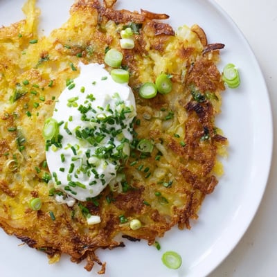 A platter of crispy Potato Cakes with Scallions and Sour Cream, topped with a dollop of sour cream.